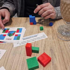 Persona resolviendo un reto de Perfiles Rompecocos con prismas 3D de colores y cartas de desafío.